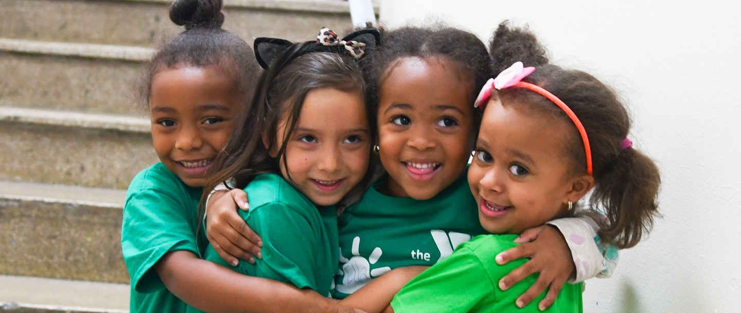 Four girls hug in hallway of Harlem YMCA during summer camp