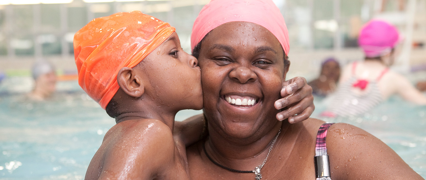 A mother and her child swim in a YMCA pool.