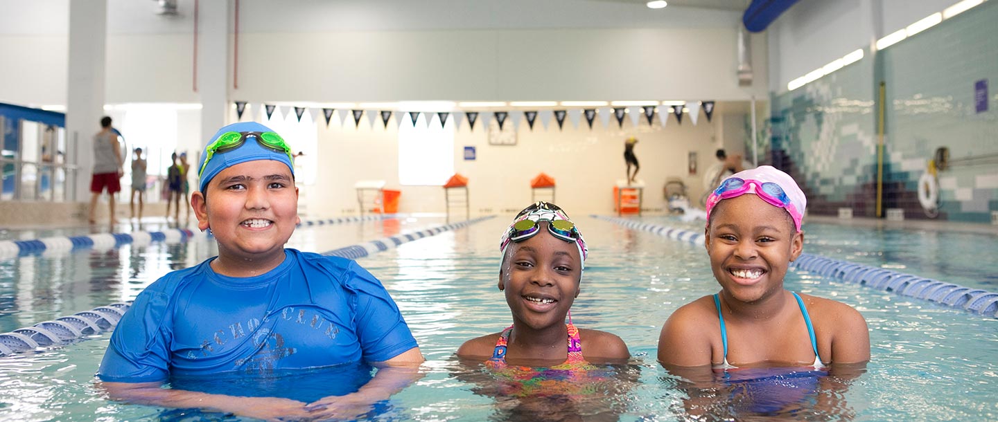 Three kids learning to swim in lap lane of indoor YMCA pool