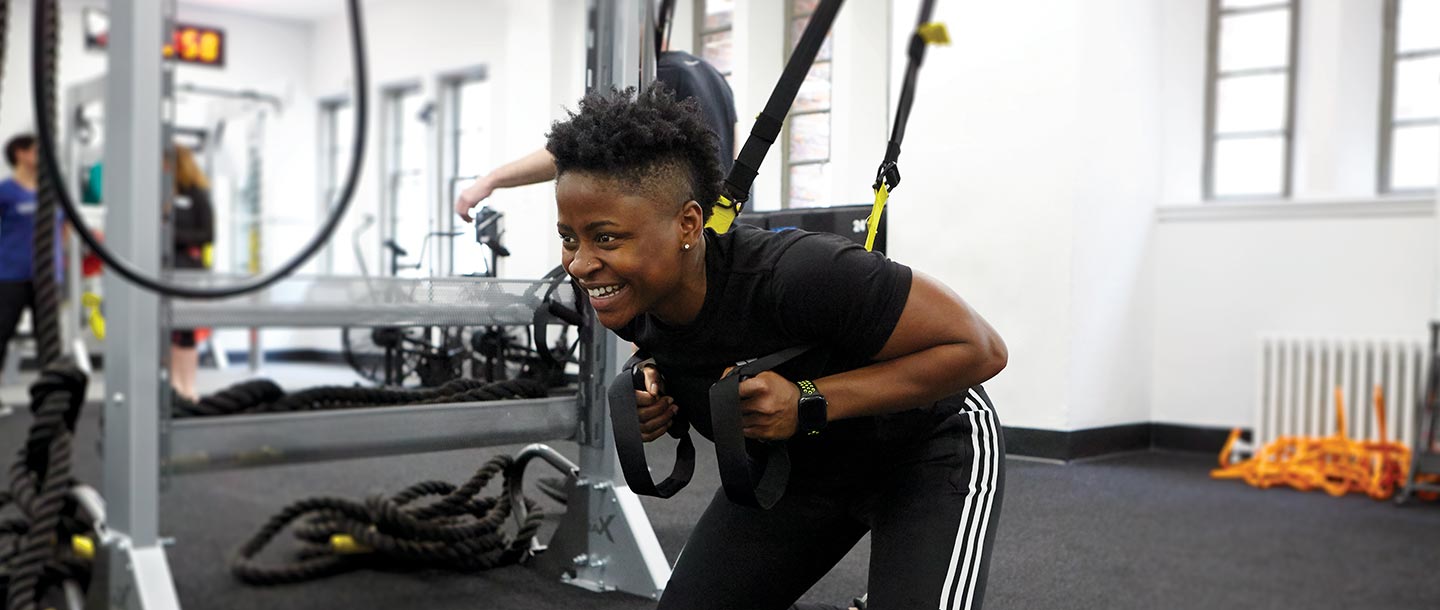 YMCA instructor demonstrates how to squat with TRX equipment during fitness class at YMCA gym