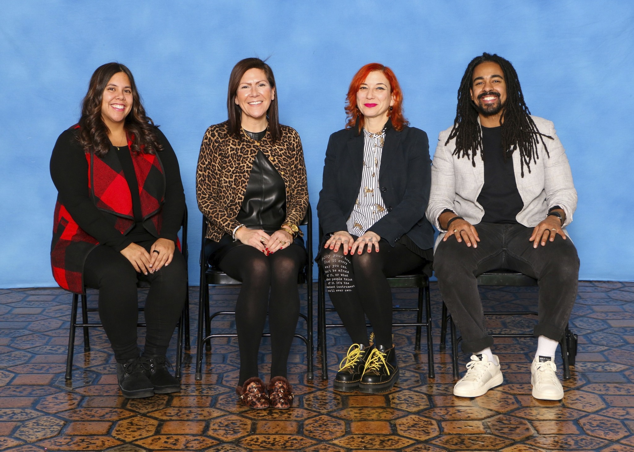 three women and one man sitting against blue wall