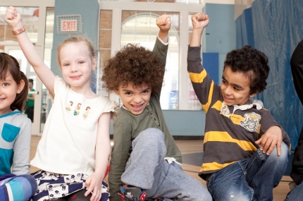 A diverse group of kids smile and raise their fists.