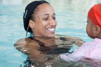 Private lesson swim instructor teaching young girl to swim in pool at YMCA