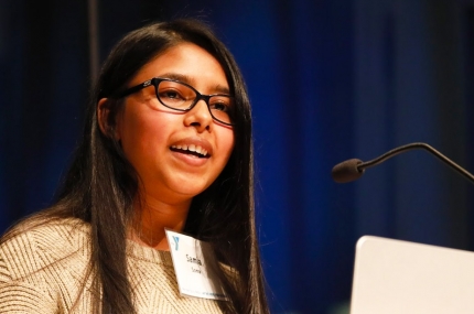 A young hispanic woman speaking at a podium.