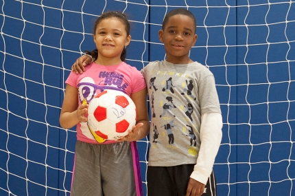 Two kids standing in front of a soccer goal.