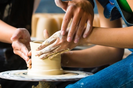 Hands working at a pottery wheel.