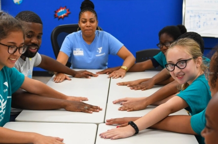 Teen campers sit at a table with their hands stretched out at the Vanderbilt YMCA camp.