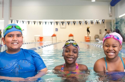 Three kids learning to swim in lap lane of indoor YMCA pool