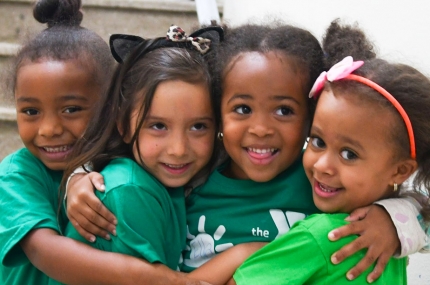 Four girls hugging and smiling at Harlem YMCA day camp in the summer