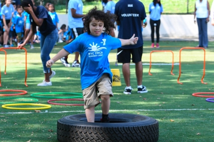 Boy playing at YMCA day camp in obstacle course outside park in Brooklyn
