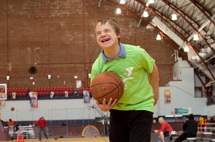 Boy in green t-shirt holding basketball at YMCA indoor gymnasium