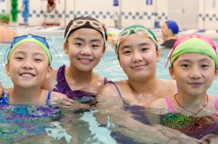 Four girls with swim caps swimming in YMCA indoor pool