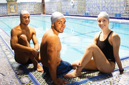 Three swimmers sit on side of West Side YMCA indoor pool
