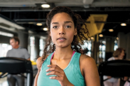 Woman in green tank top running on treadmill at gym