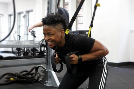 Instructor demonstrates a squat with TRX equipment in fitness class at YMCA gym