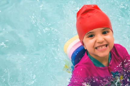 Preschool girl holding on to side of pool during swim class