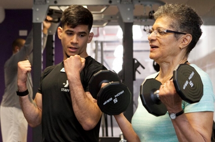 Personal trainer demonstrates how to lift weights with client at YMCA