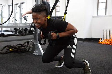 YMCA instructor demonstrates how to squat with TRX equipment during fitness class at YMCA gym