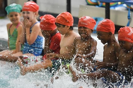 YMCA summer campers sitting on side of pool splashing water with their feet