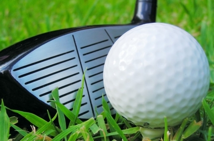 Golf ball on tee with club on green grass