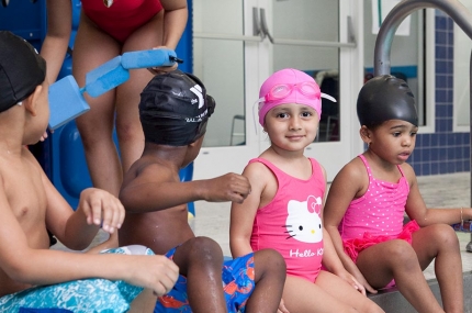 Preschoolers sitting on the side of YMCA indoor pool before swim class