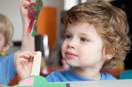 Boy holding popsicle stick craft project at Brooklyn YMCA class for kids