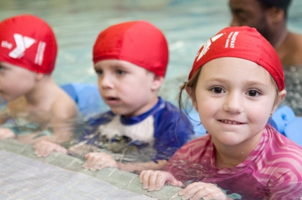 Preschoolers holding on the side of YMCA indoor pool before swim class