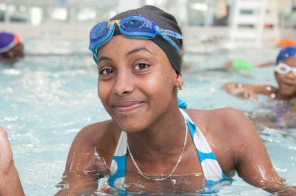 Teen girl gives thumbs up while swimming at Rockaway YMCA indoor pool in Queens