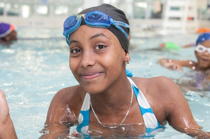 Teen girl gives thumbs up while swimming at YMCA indoor pool