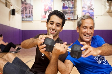 Two adult men passing weight to each other during fitness class in YMCA gym in Brooklyn