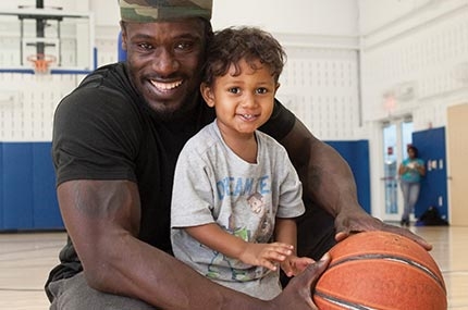 Man holding basketball and toddler son and smiling in YMCA indoor gymnasium