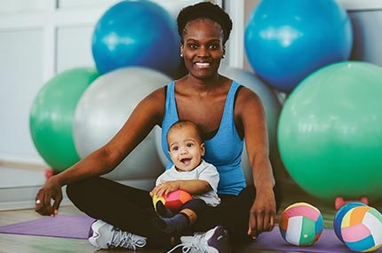 Mom sitting on yoga mat with baby and exercise balls