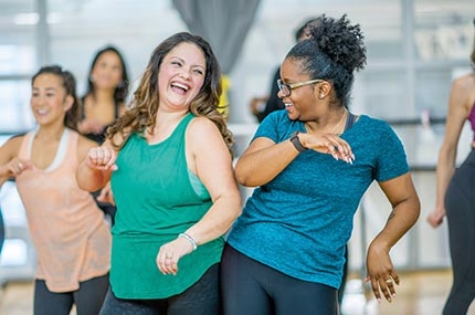 Two women smiling and bumping hips in group fitness dance class