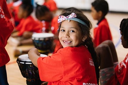 Girl with headband smiling while playing drums at Castle Hill YMCA 