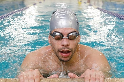 Man with goggles and swim cap takes breath at edge of North Brooklyn YMCA indoor lap swimming pool