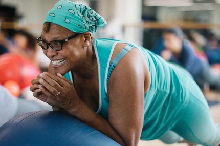 Woman with aqua bandana smiles while doing core exercises during Rockaway YMCA pilates mat class