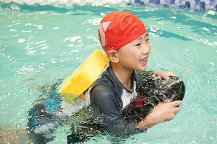 Boy with backpack and kickboard learns to swim at Vanderbilt YMCA summer camp