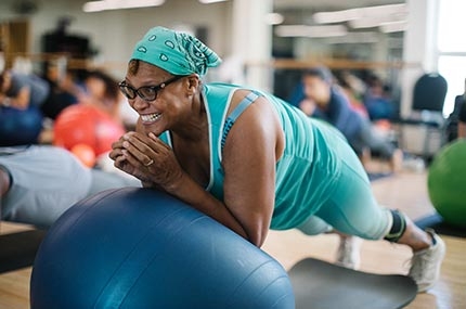 Woman with aqua bandana smiles while doing core exercises during Rockaway YMCA pilates mat class