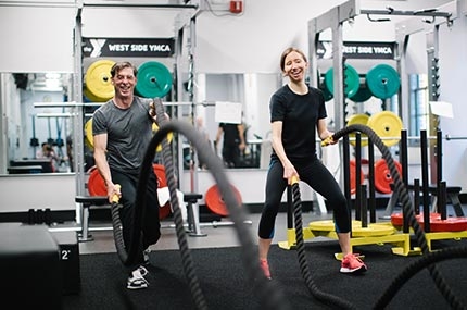 Man and woman training with battle ropes in circuit fitness class at West Side YMCA