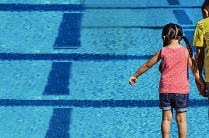 Two kids stand at the edge of the pool, looking into the water.