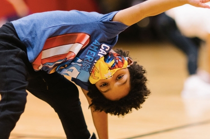 A boy wearing a mask does a yoga pose at the YMCA.