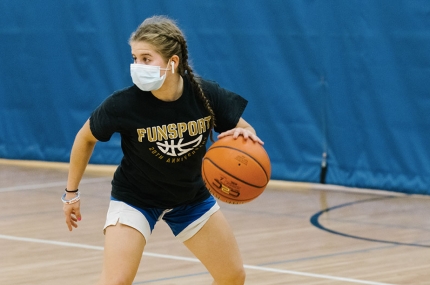 A girl in a mask plays basketball at the YMCA.