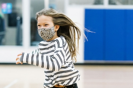 A girl runs in a large gym during a YMCA camp or learning lab.