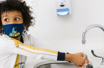 A boy in a mask washes hands at the YMCA.