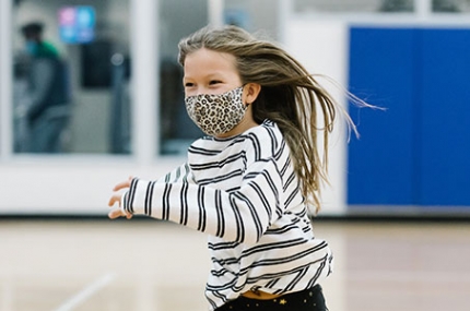 A girl in a mask runs and smiles at the YMCA.