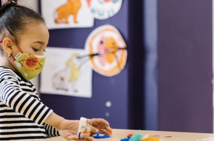A girl in a mask doing arts and craft at YMCA camp.