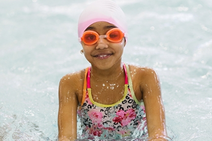 A girl posing for a picture in the pool with goggles and swim cap on