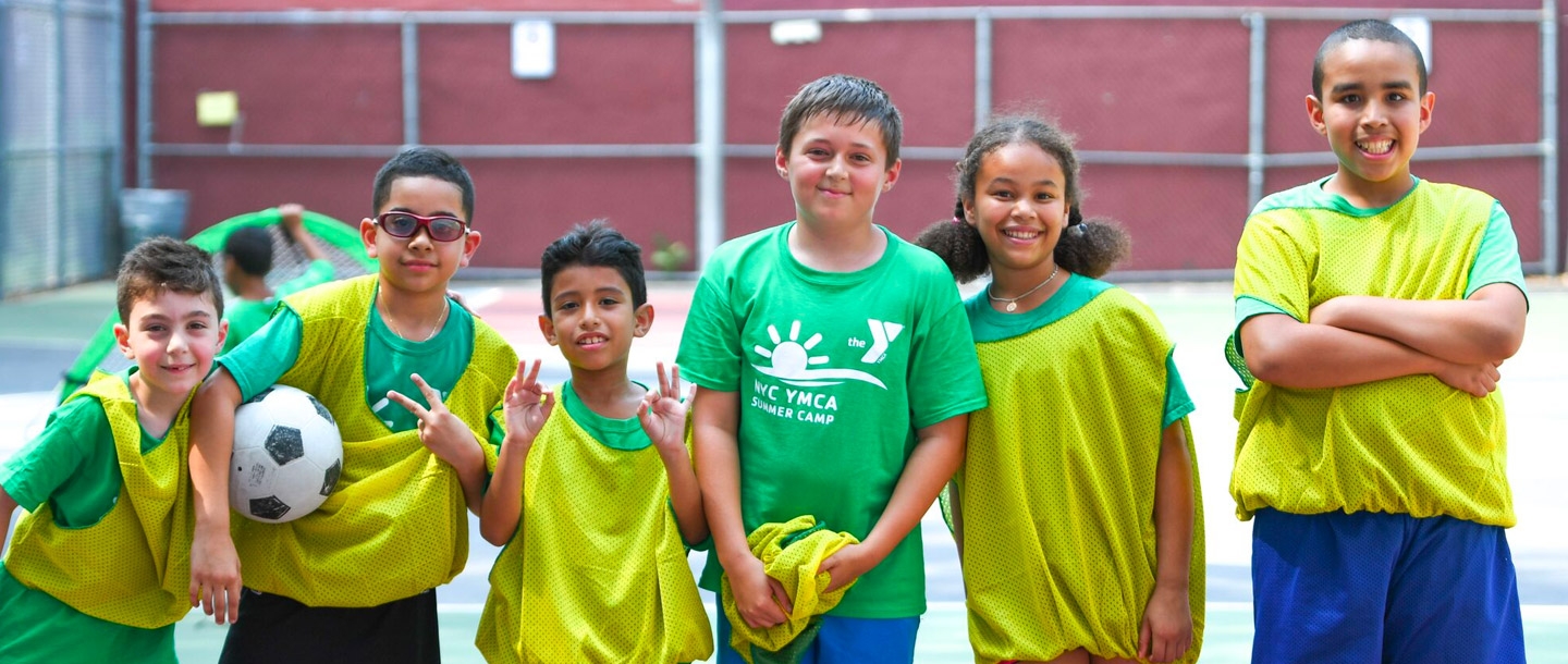 A group of kids pose with a soccer ball at a YMCA camp.