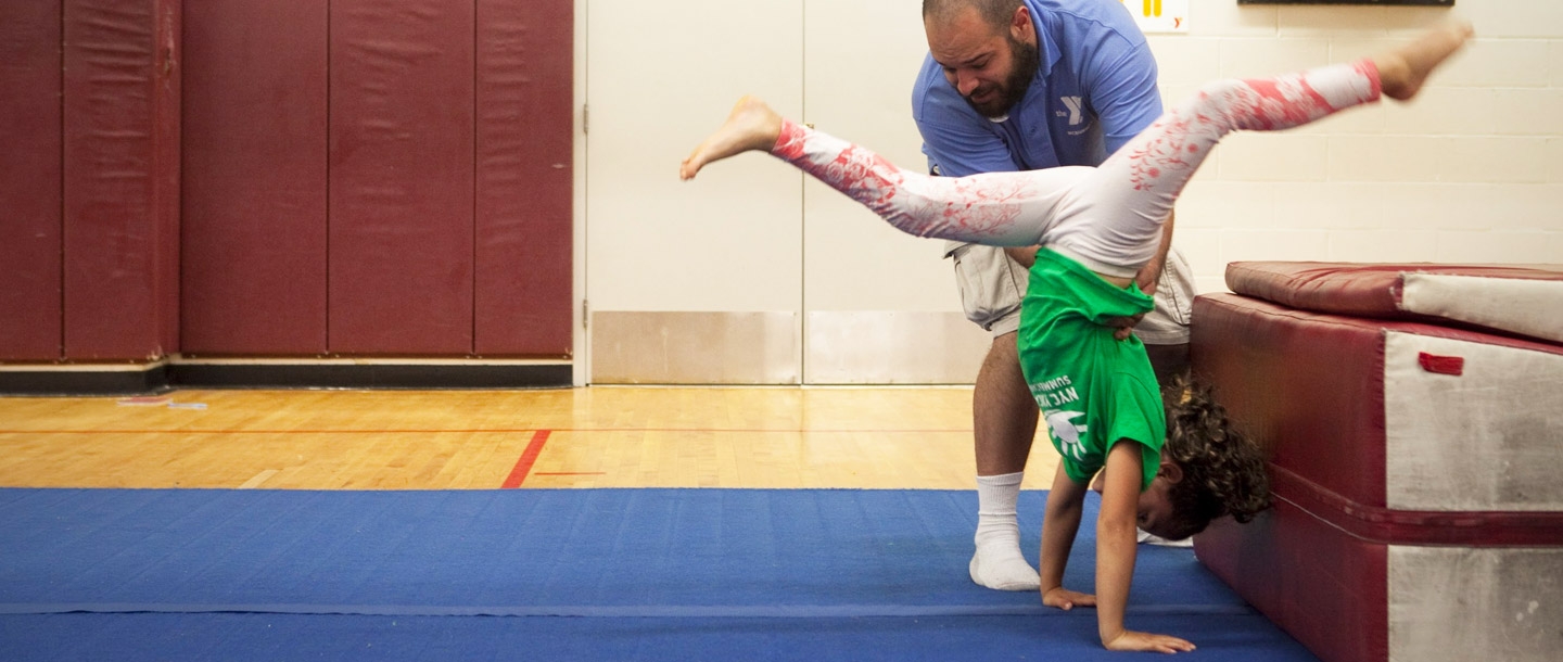 A camp counselor helps a child do gymnastics at the McBurney YMCA summer camp.