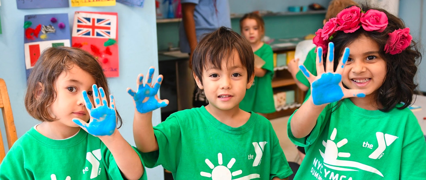 Three kids hold up paint-stained hands at the McBurney YMCA summer day camp.